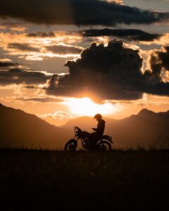 A stunning silhouette of a lone motorcyclist against a dramatic sunset and rural landscape.