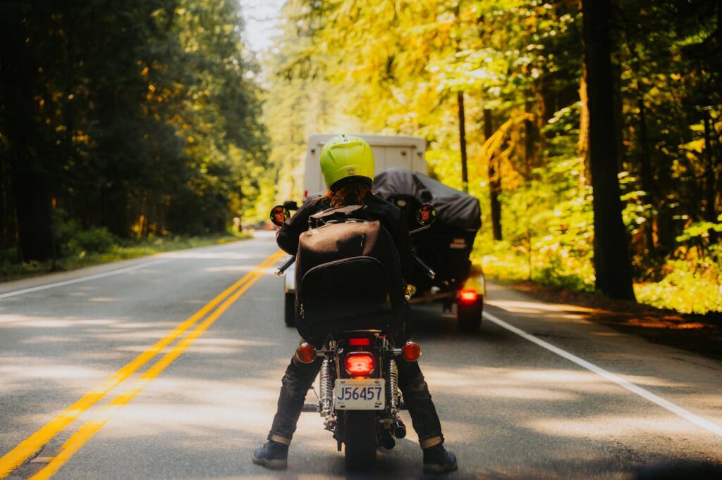A motorcyclist waits on a scenic forest road, wearing a bright yellow helmet, showcasing adventure and travel.